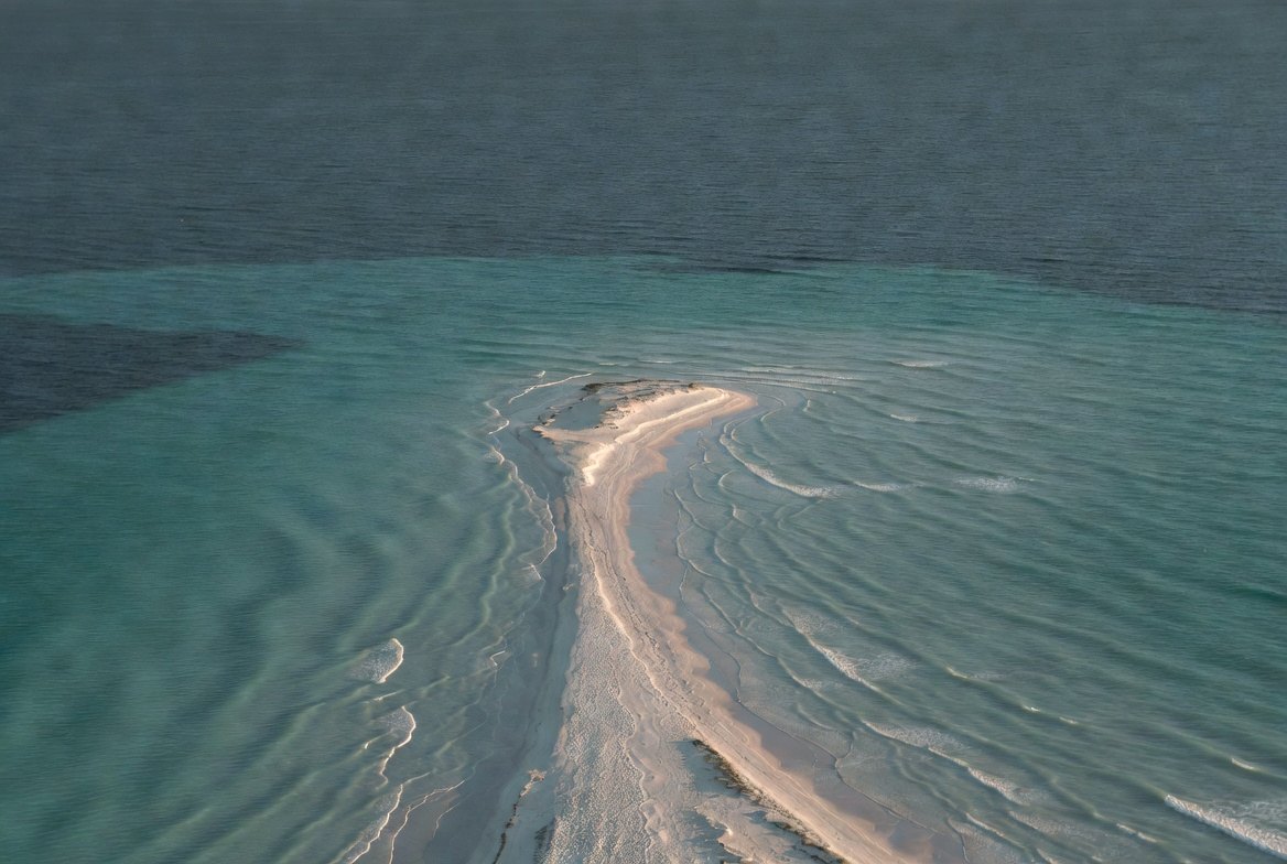 Aerial view of a pale sand peninsula meeting turquoise shallow sea